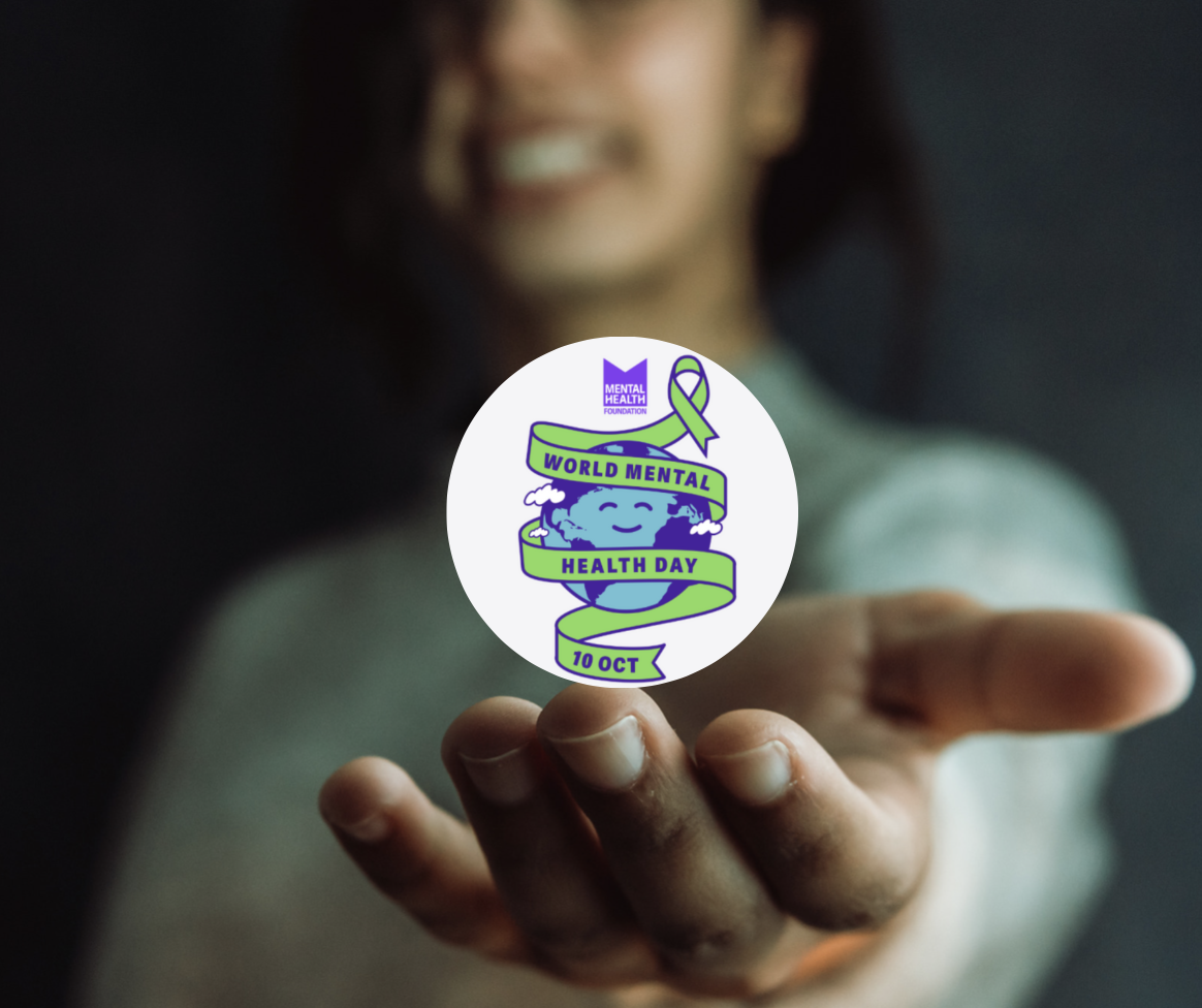 A person holds a round sticker that reads World Mental Health Day 10 Oct with a smiling globe, ribbon, and purple flag in the design.
