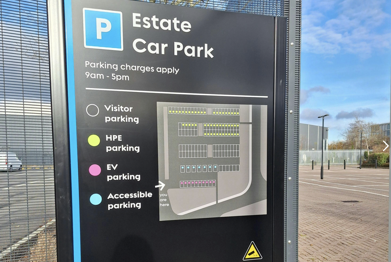 Parking sign showing a map of the Estate Car Park with designated areas for visitor, HPE, EV, and accessible parking. Parking charges apply from 9am to 5pm.